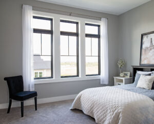 The bedroom of a home with a wall of three separate window panels class=