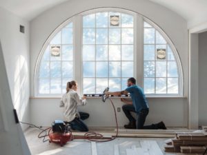 A pair of window installation specialists take measurements of a specialty window in a home