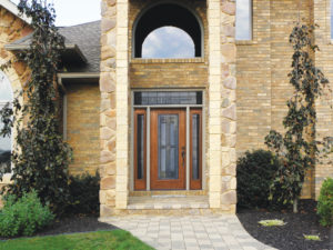 The dramatic front entryway of a home with stone siding and a wood front door