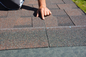 A roofer is nailing down new asphalt roof shingles 